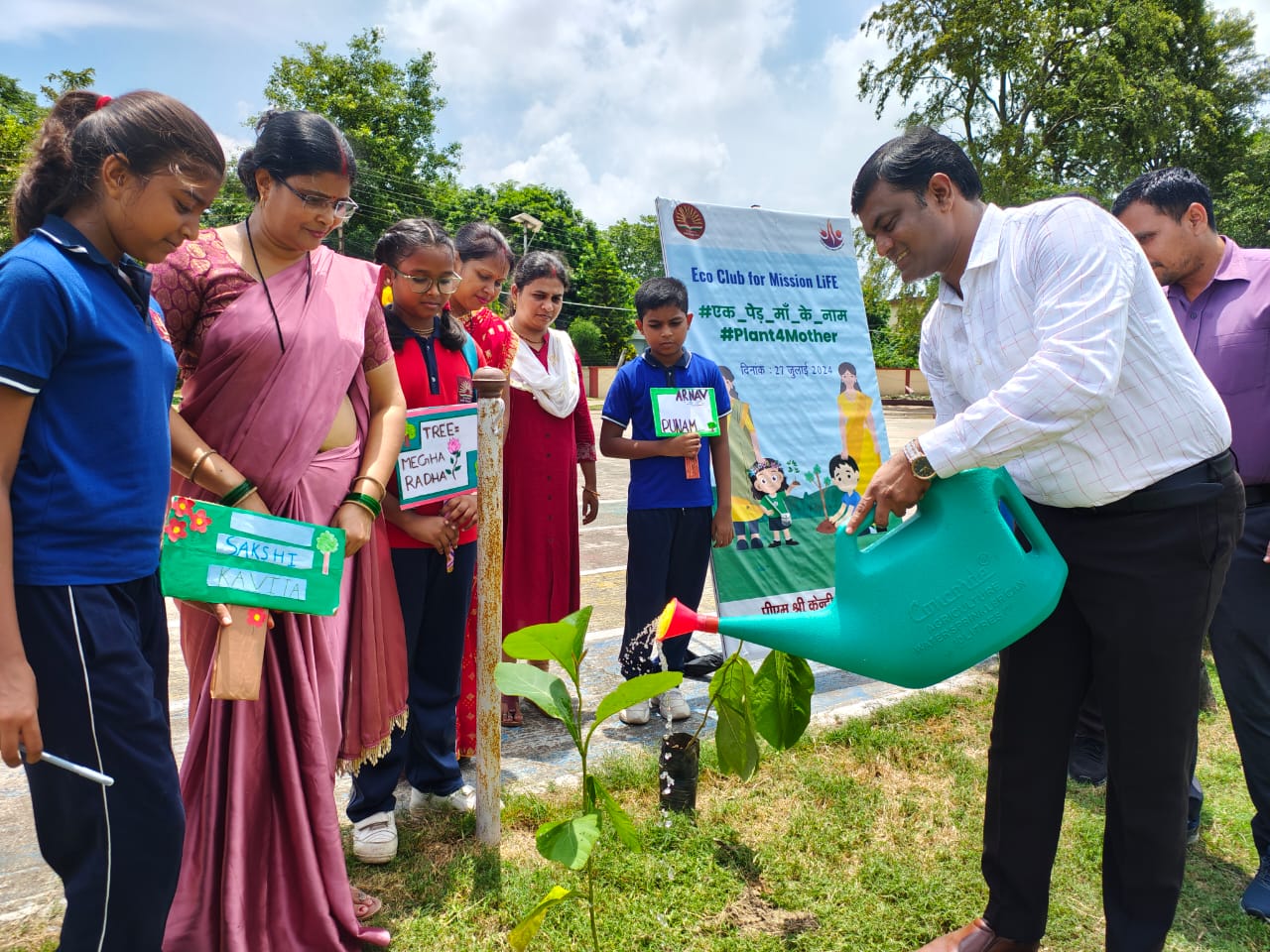 Students and teachers watering a newly planted sapling